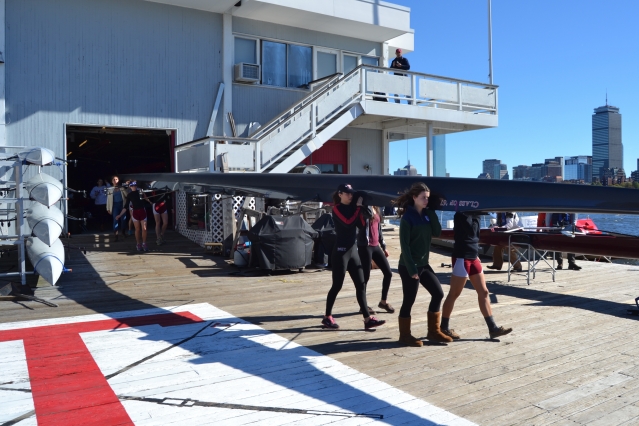 Members of the Varsity 8 lineup prepare for race time. Valerie Hunter (front left) and Kelly Barton carry bow 39, a 200-pound boat, with help from Michelle Lauer (back left) and Sylvia Sarnik. Navigating the shell across the busy dock isn’t easy but directives like, “Ready up in the bow, swing to Boston,” get the job done. (Photo: Sam Hunter Magee/Arts at MIT)